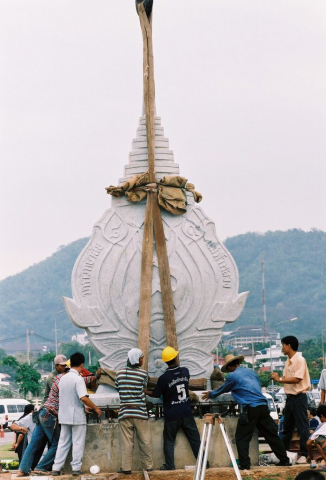 คนงานกำลังยกศิลาตราสัญลักษณ์ไว้บนแท่นฐาน